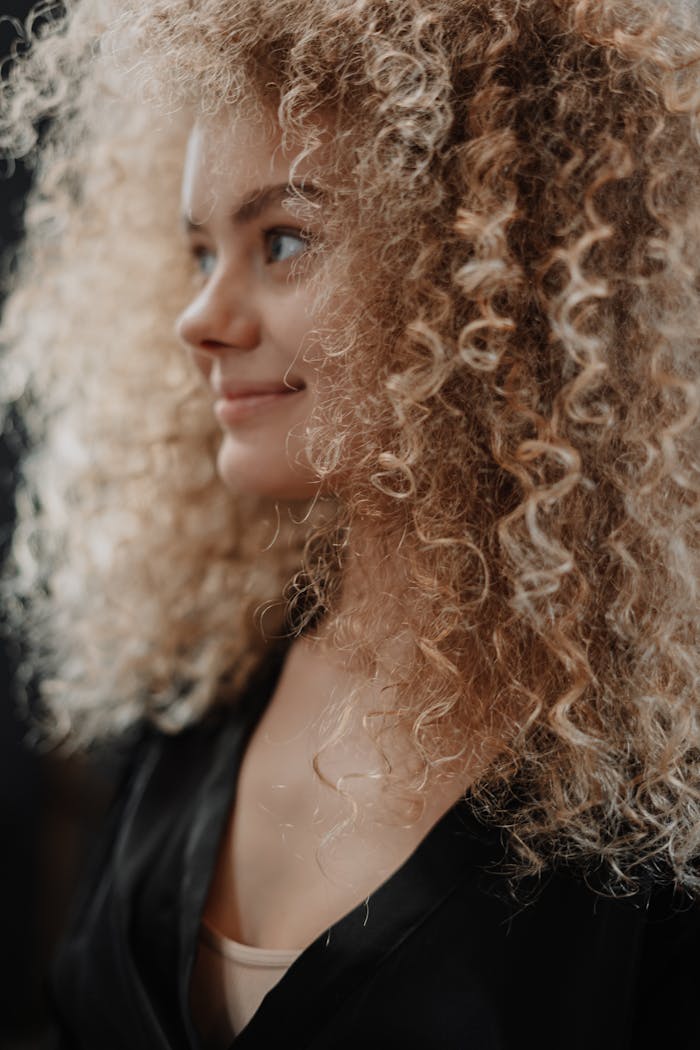 Tips para mantener tu cabello sano Smiling young woman with natural curly hair in profile portrait.